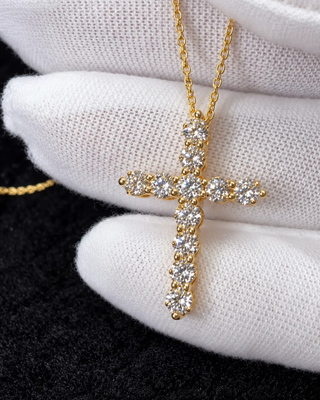Gold cross pendant set with round diamonds, held in a jeweler's glove