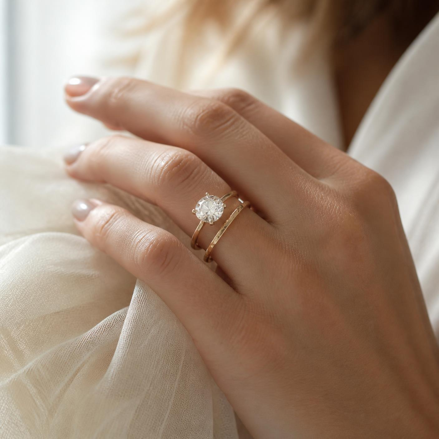 Hand wearing a diamond engagement ring with a thin gold band